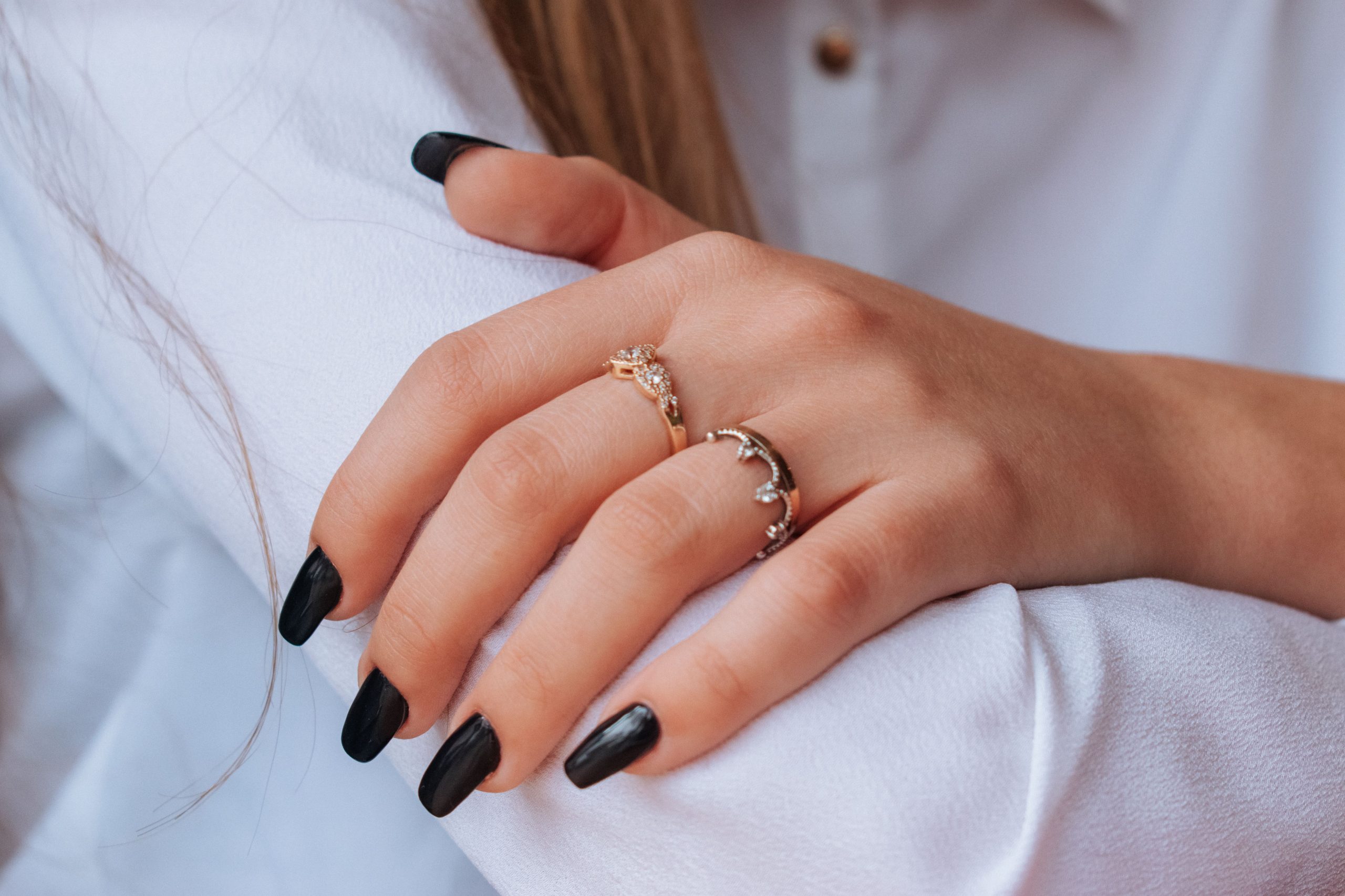Mains avec vernis noir et bagues élégantes sur chemise blanche