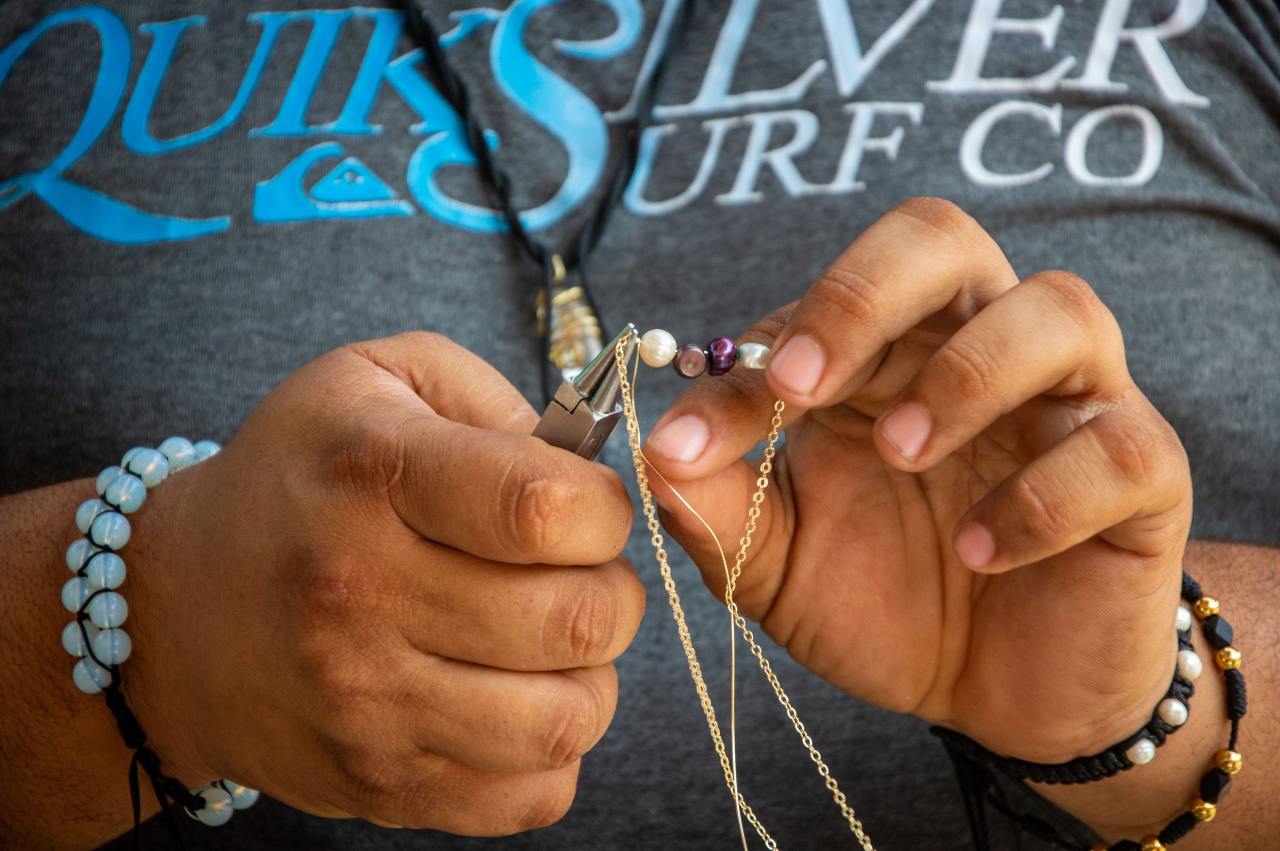 Mains créant bijoux artisanaux avec perles chaînes.