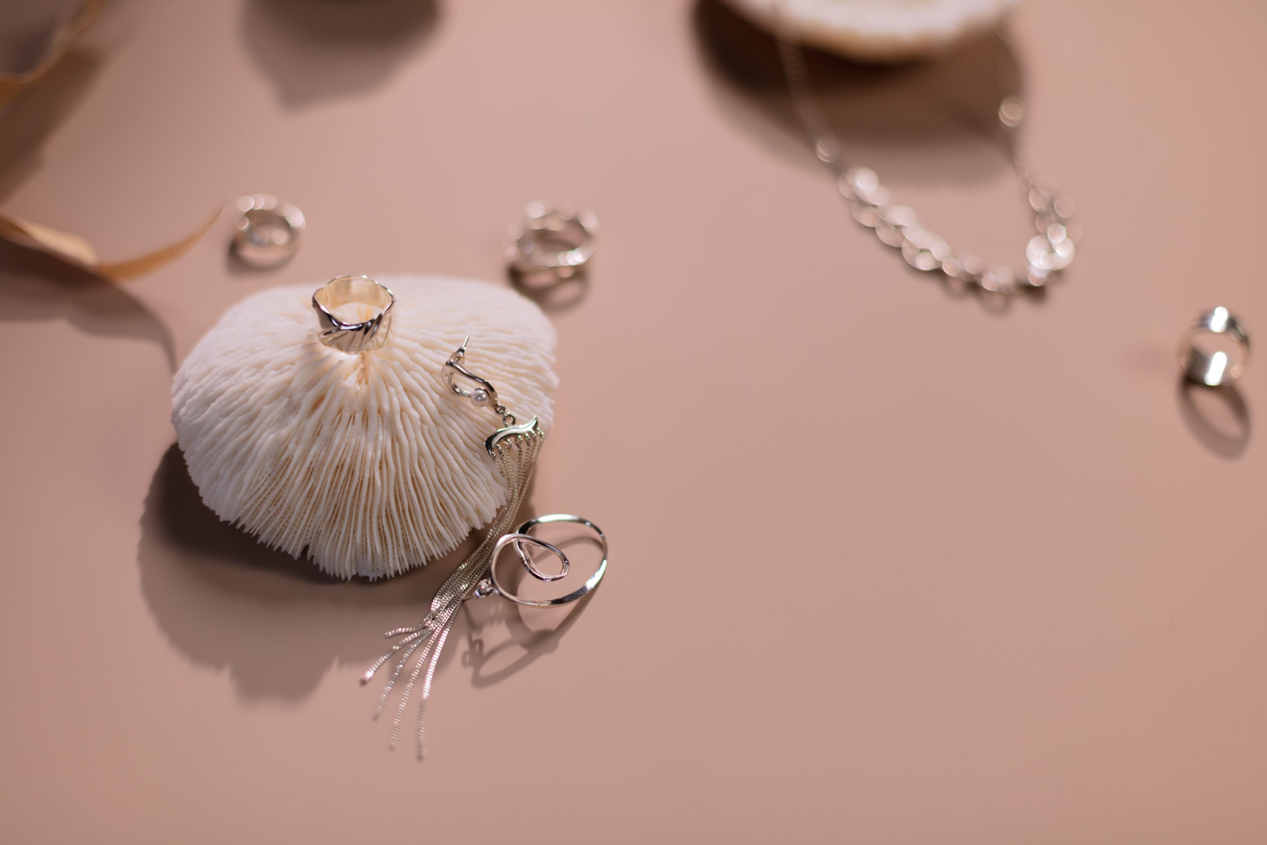 Bagues et collier argentés sur fond rose
