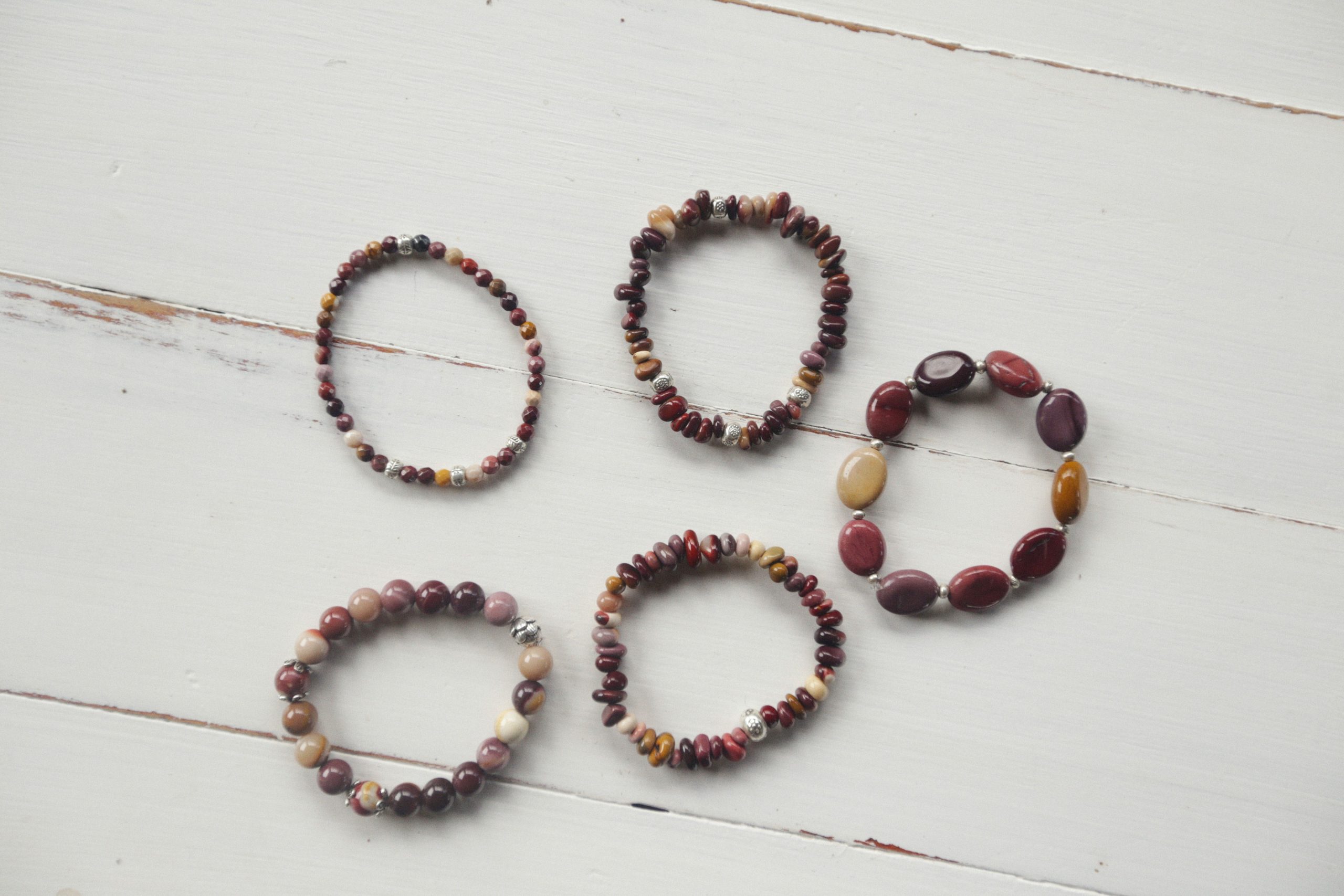 Cinq bracelets perlés sur table bois blanc